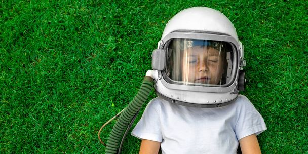 A child lies on the grass wearing an astronaut's helmet and dreams of great achievements! - Фото, изображение