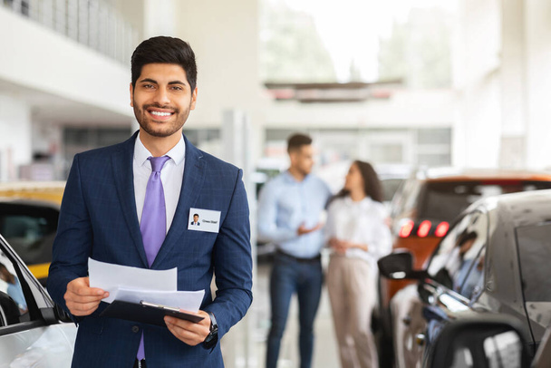 Charismatische Arabisch man sales assistent poseren over auto showroom - Foto, afbeelding