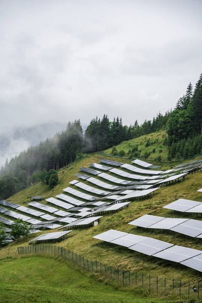 Güneş, fotovoltaik güç istasyonu Alplerdeki bir dağ yamacında. Sisli bir gün, yeşil çayır çimen ve mavi gökyüzü ve dağlar taze ve ekolojik bir görüntü yaratır.. - Fotoğraf, Görsel