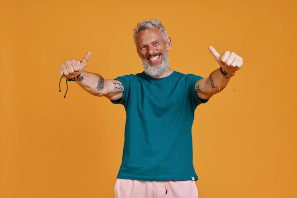 Happy senior man showing his thumbs up while standing against orange background - Foto, Bild