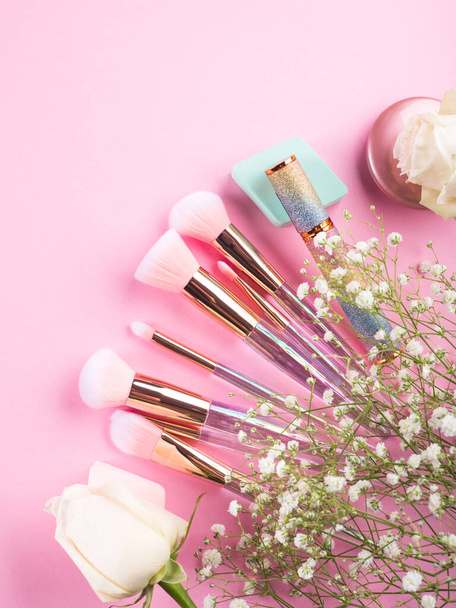 Trendy make up brushes with products on pink background with gypsophila flowers - Photo, Image