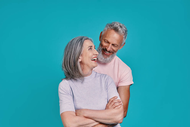 Heureux couple aîné coller et sourire tout en se tenant ensemble sur fond bleu - Photo, image