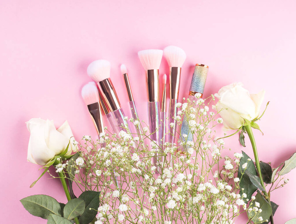 Модні макіяжні пензлі з продуктами на рожевому тлі з квітами гіпсофіли
 - Фото, зображення