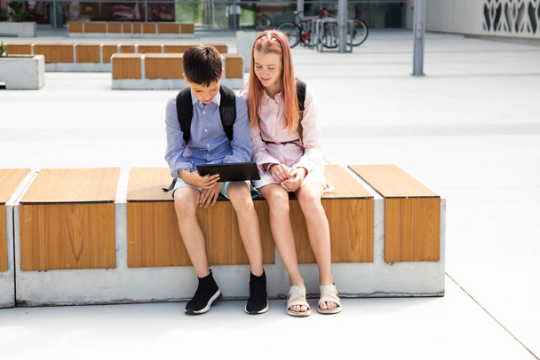 Zdjęcie dwójki nastoletniego rodzeństwa korzystającego z tabletu cyfrowego w pobliżu szkoły, odrabiającego lekcje - Zdjęcie, obraz