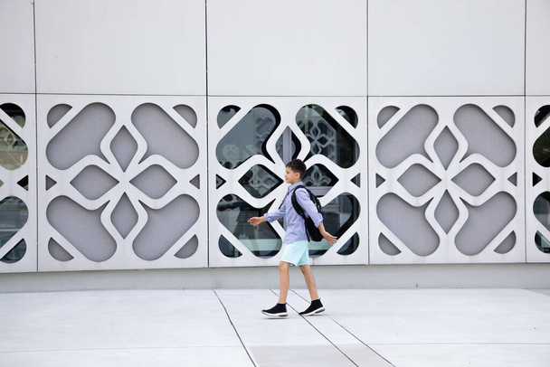 Ένα σχολιαρόπαιδο με σακίδιο περπατάει σε τσιμεντένιο τοίχο κτιρίου. Αντιγραφή χώρου για κείμενο - Φωτογραφία, εικόνα
