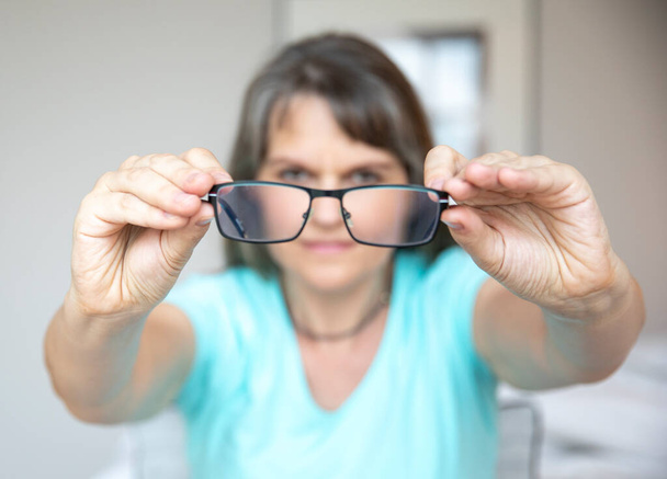 Orta yaşlı bir kadın daha iyi görebilmek için gözlüklerini düzeltiyor. - Fotoğraf, Görsel