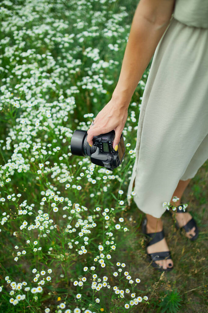 Жінка-фотограф тримає камеру на відкритому повітрі на квітковому полі, невідома жінка тримає цифрову камеру в руках. Фотографія природи подорожей, простір для тексту
. - Фото, зображення