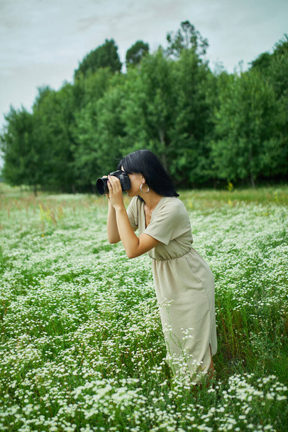 Жінка-фотограф фотографує на відкритому повітрі на квітковому полі, тримаючи камеру, жінка тримає цифрову камеру в руках. Фотографія природи подорожей, простір для тексту, вид зверху
. - Фото, зображення