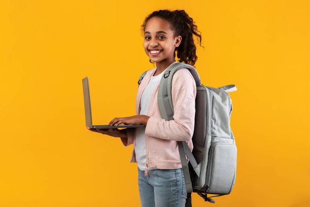 zwart meisje staan met personal computer in gele studio - Foto, afbeelding