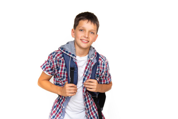 Chłopiec nastolatek 11 lat uczeń patrząc w aparat fotograficzny na białym tle z plecakiem i uśmiechem. Ubrany w koszulę w kratę i biały t-shirt - Zdjęcie, obraz