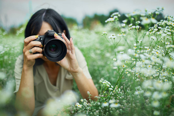 Portrét fotografky fotografovat venku na květinové louce krajiny s fotoaparátem, žena drží digitální fotoaparát v ruce. Cestovní příroda fotografie, prostor pro text, horní pohled. - Fotografie, Obrázek