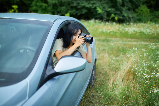 Γυναίκα φωτογράφος κάθεται στο αυτοκίνητο και φωτογραφίζοντας ένα τοπίο στον τομέα των λουλουδιών, ταξιδεύουν θηλυκό τραβήξτε φωτογραφία, χώρος για κείμενο. - Φωτογραφία, εικόνα
