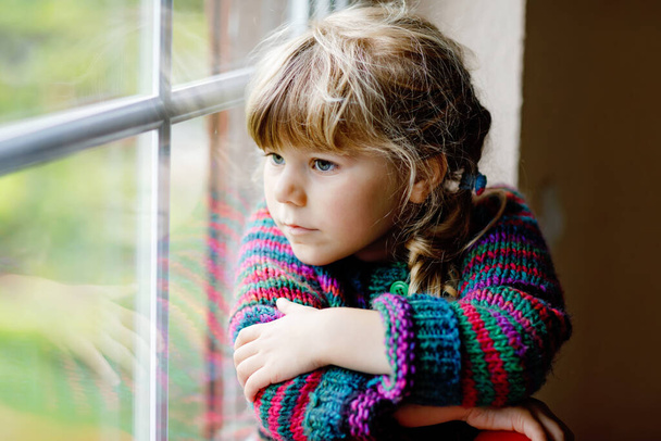 Petite fille assise près de la fenêtre. Enfant d'âge préscolaire porter confortable pull en laine auto-tricoté. Tout-petit regardant sous la pluie dehors. Automne et hiver. - Photo, image