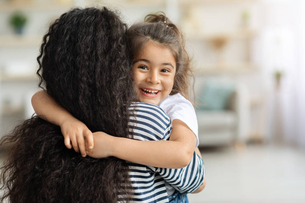 Nettes kleines Mädchen umarmt ihre Mutter und lächelt fröhlich - Foto, Bild