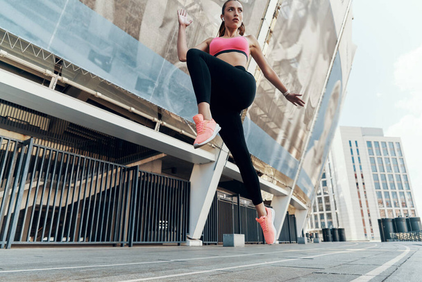 Low angle view of confident young woman in sportswear running outdoors - Foto, Bild