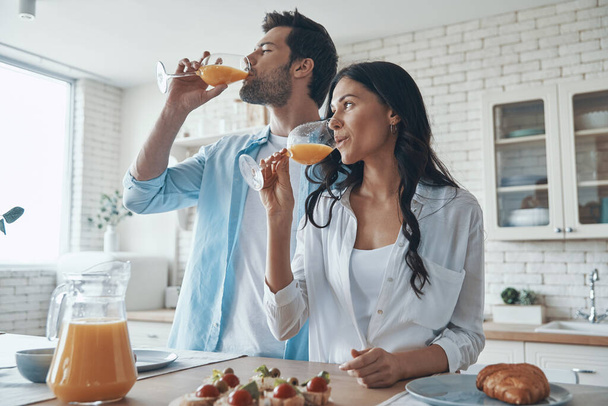 Young couple drinking orange juice while spending time in the domestic kitchen - Foto, Imagem