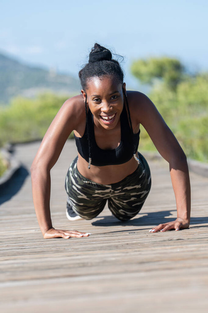 Αγώνας αφρο-αμερικανική γυναίκα κάνει πους απς σε ένα ξύλινο διάδρομο: Άσκηση και προσπάθεια έννοια. - Φωτογραφία, εικόνα