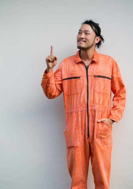 El mecánico jefe en uniforme naranja apuntando un dedo hacia arriba. Retrato sobre fondo gris con luz de estudio. - Foto, imagen