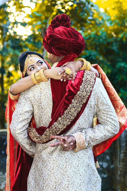 Indian wedding couple hugging and groom showing victory sign with green bokeh background.  - Foto, afbeelding