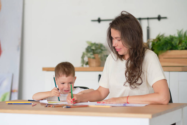 Мальчик учится рисовать. Мама и сын весело рисуют карандашами. Детское творчество. - Фото, изображение