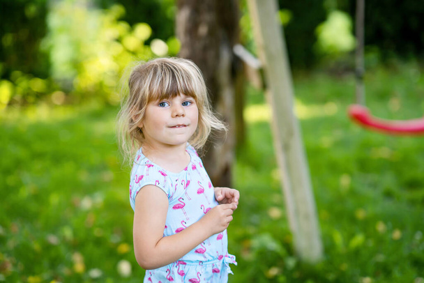 Portrait of happy smiling toddler girl outdoors. Little child with blond hairs looking and smiling at the camera. Happy healthy child enjoy outdoor activity and playing. - Photo, image
