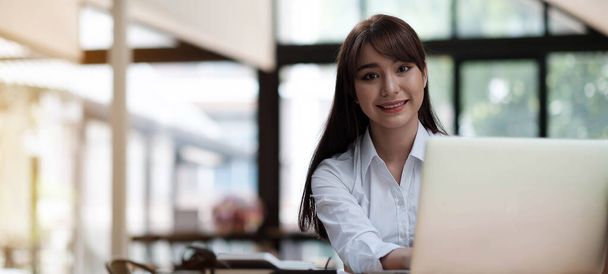 Portrait of a cheerful businesswoman sitting at the table in office and looking at camer - Photo, image
