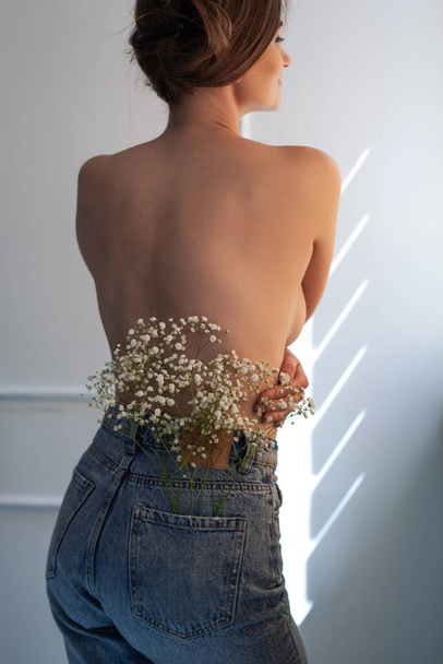 white little flowers in jeans back pocket weared on A girl with beautiful healthy naked back. - Foto, Imagem