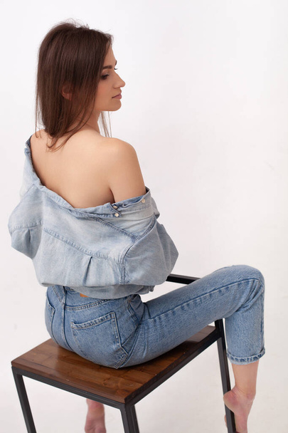 Luxury lady in a shirt and blue jeans with open back and shoulders sitting on a bar stool gracefully turning - Foto, afbeelding