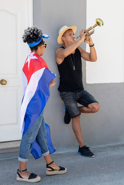 Любопытная латиноамериканка, наблюдающая за латиноамериканцем, играющим на трубе: избирательный фокус. Искусство и разнообразие. - Фото, изображение
