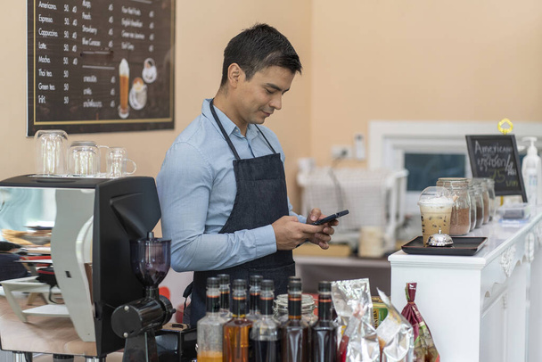 Ο ιδιοκτήτης μιας καφετέριας barista απαντά στο τηλέφωνο για να παραλάβει την παραγγελία. Από τους πελάτες και να έχουν barita προετοιμάσει καφέ σε μια καφετέρια  - Φωτογραφία, εικόνα