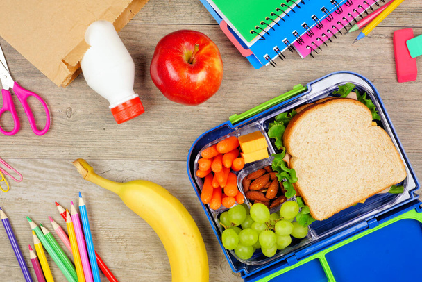 Almoço escolar saudável e material escolar. Vista superior sobre um fundo de madeira. - Foto, Imagem