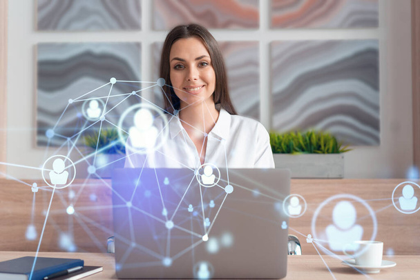 Attractive businesswoman in white shirt at workplace working with laptop to hire new employees for international business consulting. HR, social media hologram icons over office background - Photo, image