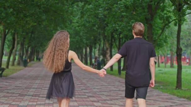 una pareja joven, un chico y una chica están corriendo por el callejón en el parque, abrazándose, tonteando, mostrando sentimientos el uno al otro. - Metraje, vídeo
