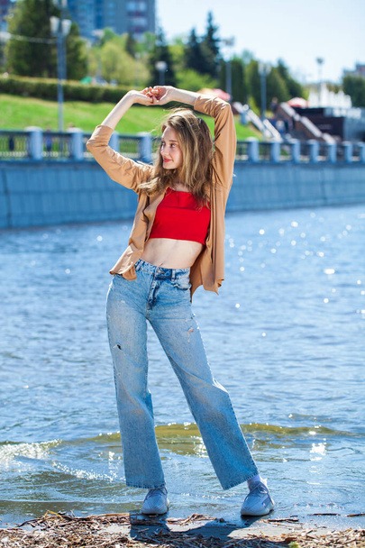 Full length portrait of a young stylish girl in a beige blouse with long sleeves and blue jeans - Foto, Bild