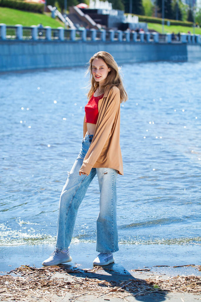 Full length portrait of a young stylish girl in a beige blouse with long sleeves and blue jeans - Photo, Image
