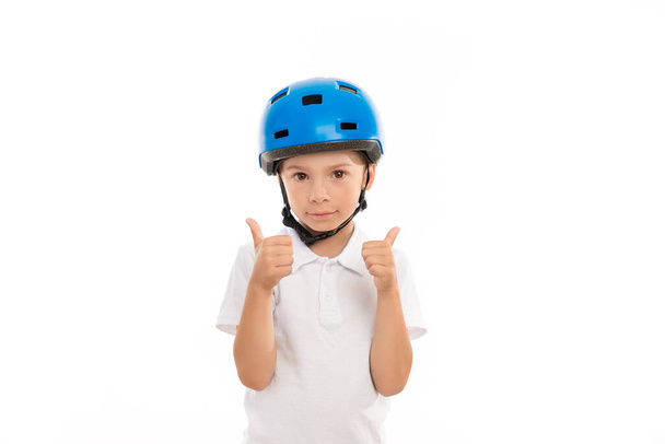 A boy in a blue helmet shows a gesture of big hands up, he does not smile, a calm expression on his face. Stands on white isolated background - Foto, Bild