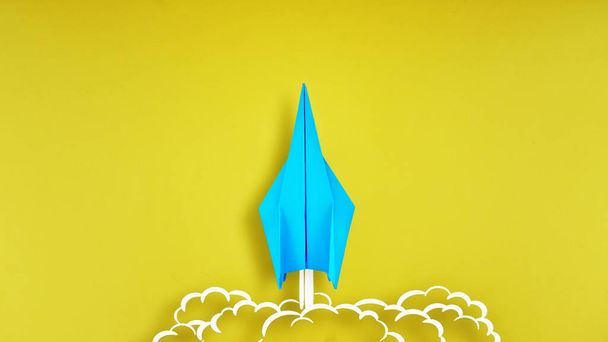 Blue origami plane on yellow background with smoke coming out from aircraft tails - Photo, Image