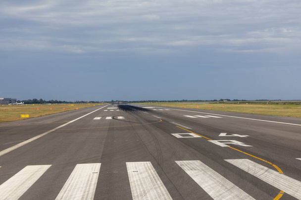 злітно-посадкова смуга аеропорту з хмарним небом і друком коліс на поверхні
 - Фото, зображення