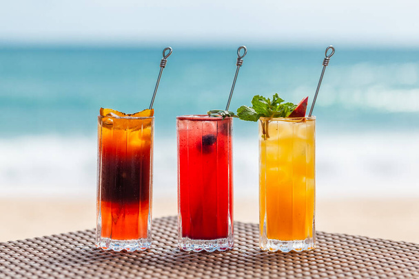 Set of Refreshing Fruit Cocktails Standing on Table on Beach near Turquoise Sea - Fotoğraf, Görsel