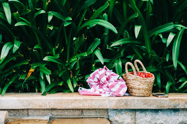Towel and basket with swimming and sunbath accesories on the stone ledge by the pool in the tropics. nobody - Fotoğraf, Görsel