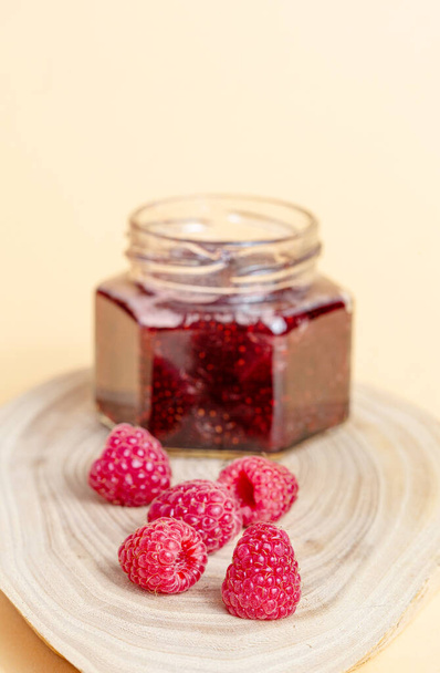 Raspberry jam in a jar on a wooden cut, next to there are raspberries - Foto, immagini