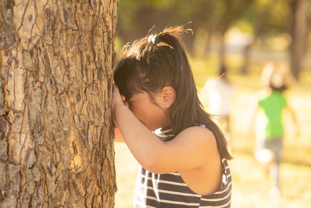 little girl is playing hide-and-seek hiding face in the park - Foto, imagen