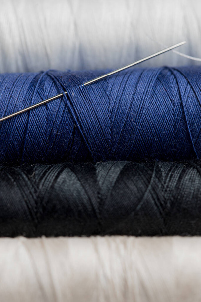 Μακρο φωτογραφία του νήματος για ράψιμο σε ένα καρούλι μαύρο άσπρο και μπλε χρώμα με βελόνα - Φωτογραφία, εικόνα