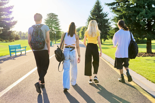Egy csapat tinédzser barát a napos nyári napon együtt sétálnak az úton, visszapillantás - Fotó, kép