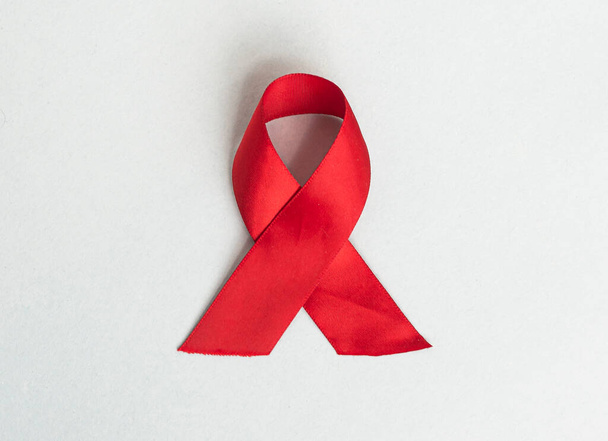 Red medical ribbon for AIDS and HIV day awareness. Curled satin bow on blue background - Φωτογραφία, εικόνα