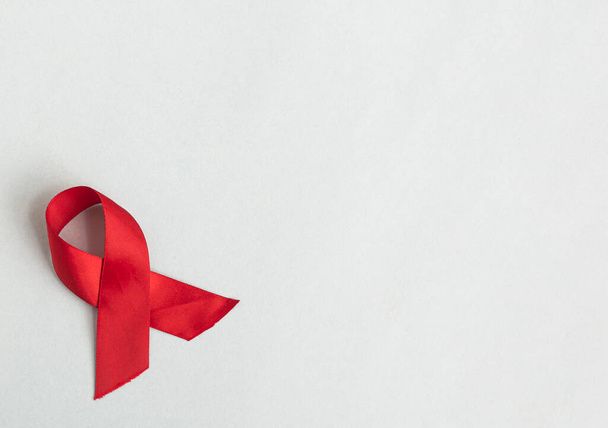 Red swirled ribbon for AIDS and HIV day on blue background. Satin bow with place for text - Фото, изображение
