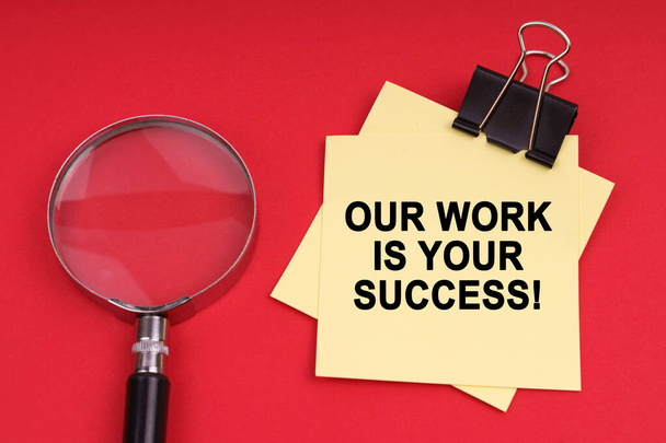 Business and Economics. On a red background, a magnifying glass and a sticker with the inscription - Our work is your success - Fotografie, Obrázek