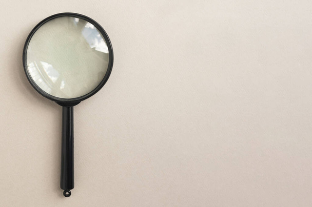 Magnifying glass over pale beige background. Magnifier as concept of finding answers - Fotoğraf, Görsel