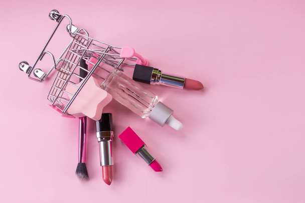 Shopping trolley with make-up products over pink background.Shopping cart with cosmetics. Online sales concept.Skincare cosmetics and lipsticks. advertising and marketing banner - 写真・画像