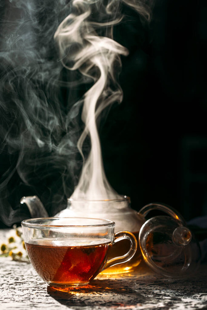 Чашка горячего чая со стеклянным чайником на тёмном фоне - Фото, изображение